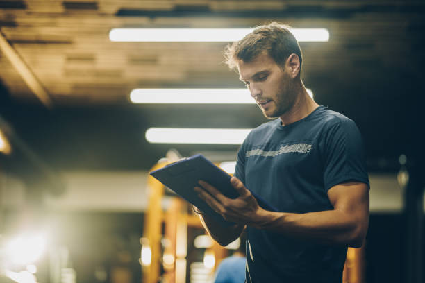 instructeur de fitness jeune lecture un plan de formation dans une salle de gym. - coach exercising instructor gym photos et images de collection