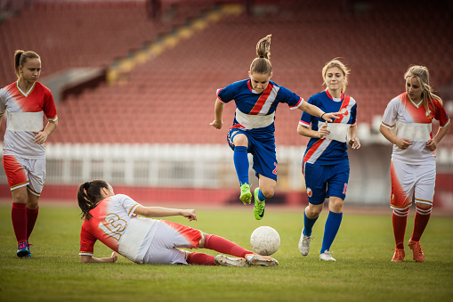 Teenage girls tackling during the soccer match on a playing field.
