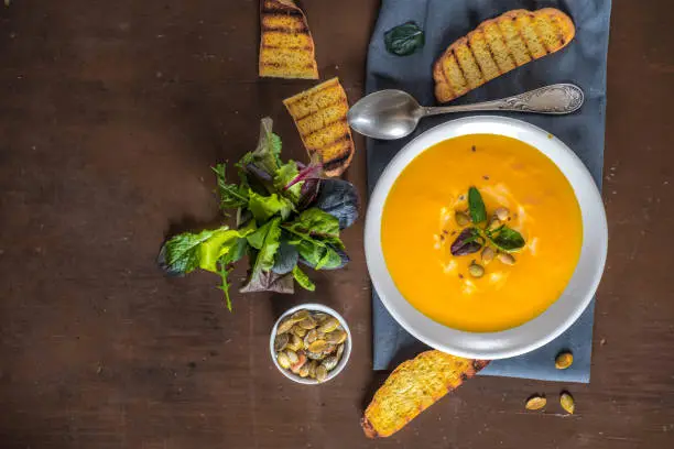 Fried pumpkin and carrot soup with cream and pumpkin seeds on a dark wooden background. Greens and pumpkins seeds
