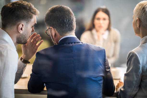 Come closer, what do you think about this candidate? Male member of human resource team whispering to his colleague during a job interview in the office. The view is through glass. mystery stock pictures, royalty-free photos & images