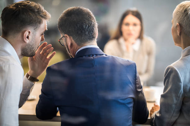 Come closer, what do you think about this candidate? Male member of human resource team whispering to his colleague during a job interview in the office. The view is through glass. whisper men stock pictures, royalty-free photos & images