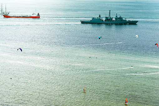 Two vessels of the NSW Water Police patrol around the exclusion zone established in Sydney Harbour for the USS Tripoli of the US Navy.  The red line in the water is a protective device around the ship. A group of five people, including one wearing an officer's uniform, stand on the deck.  The mast of HMAS Sydney, a war memorial to those who served in the Royal Australian Navy, and the ships and sailors lost, is visible on Bradleys Head.  This image was taken from Mrs Macquarie's Chair on an afternoon in Spring.