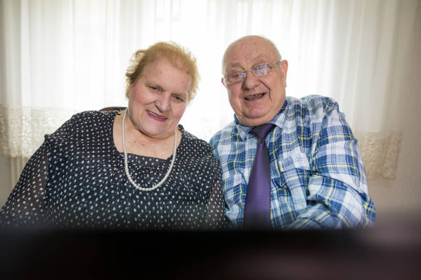 sechzig jahre zusammen. älteres paar mit laptop zu hause - overweight smiling senior women 70s stock-fotos und bilder