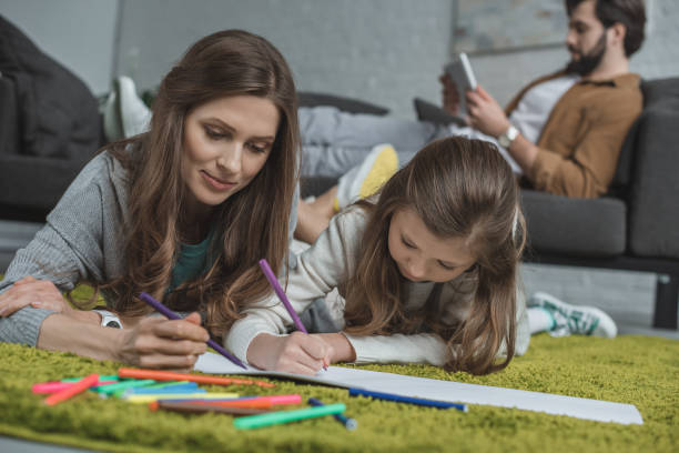 istock mother and daughter drawing on floor while father using tablet on sofa in living room 942156928