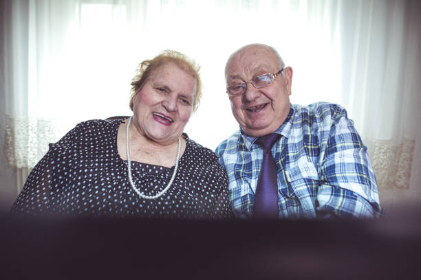 sechzig jahre zusammen. älteres paar mit laptop zu hause - overweight smiling senior women 70s stock-fotos und bilder