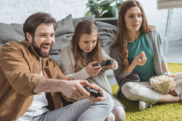 istock father and daughter playing video game and mother eating popcorn 942160468