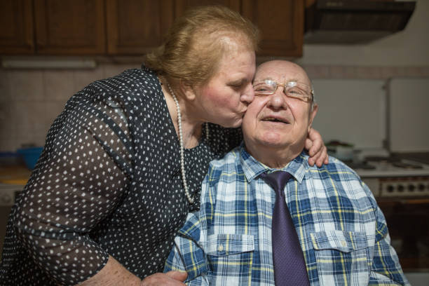ein kuss für 60 jahre ehe. gerne älteres paar im wohnzimmer - overweight smiling senior women 70s stock-fotos und bilder