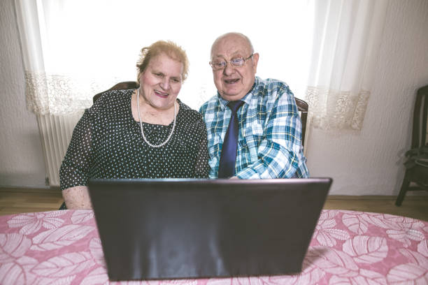 sechzig jahre zusammen. älteres paar mit laptop zu hause - overweight smiling senior women 70s stock-fotos und bilder