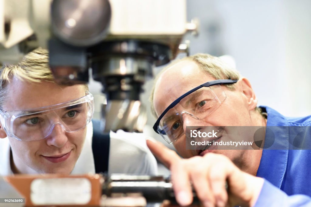 closeup picture: trainer and apprentice in vocational training on a milling machine - teacher explains details of the machine Trainee Stock Photo
