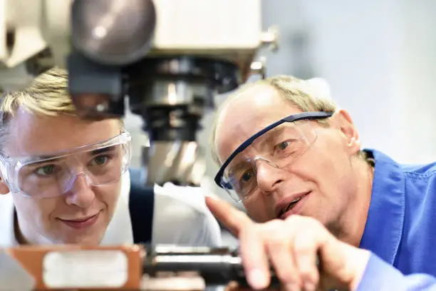 closeup picture: trainer and apprentice in vocational training on a milling machine - teacher explains details of the machine