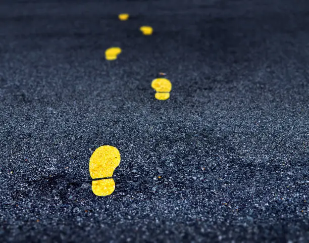 Photo of Yellow footprint signs on an asphalt road. Painted footprints show the way