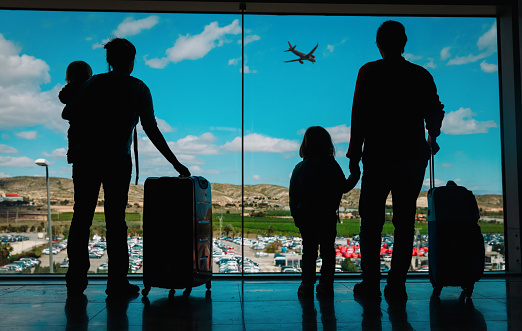 family with kids and luggage looking at planes in airport, travel concept