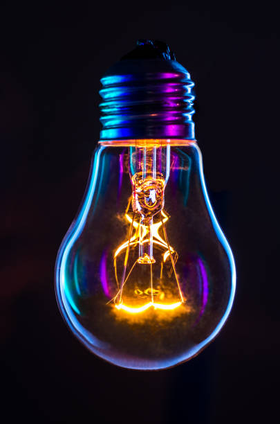 light bulb glowing with black background - single object fotos imagens e fotografias de stock