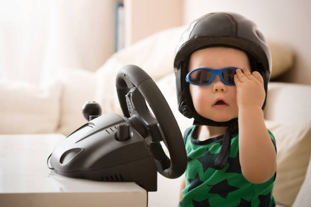 istock Cute little kid boy in a helmet playing with Computer steering wheel. Future driver. Getting ready for professional driving. Child driving a car. Funny toddler boy indoors. Boy and a car. 942180216