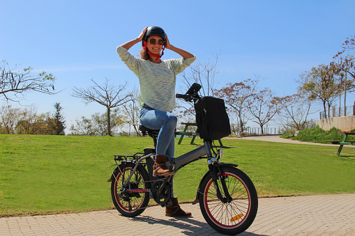 A smiling woman with electric bicycle in the park Wearing  a helmet