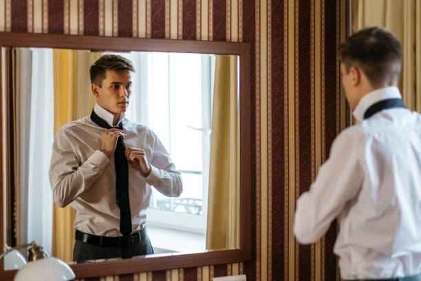 istock A young handsome man ties up a tie in front of a mirror 942180886