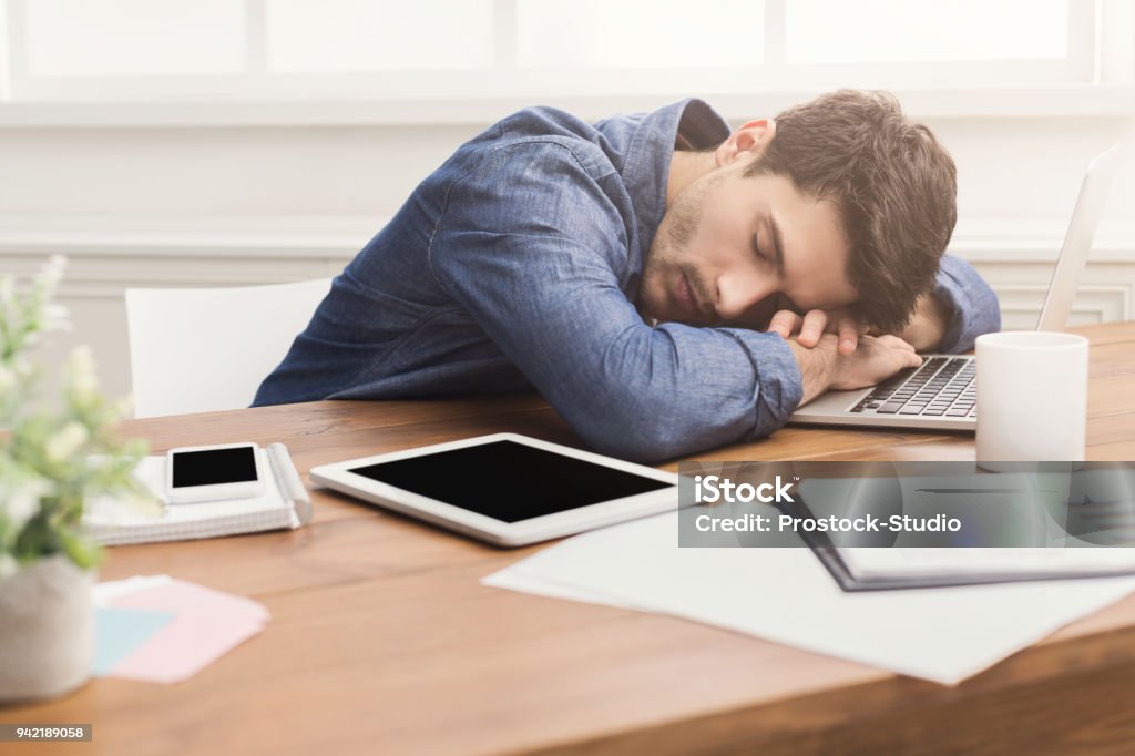 Sleeping businessman in modern office Sleep at work. Tired, overworked businessman napping at workplace in modern office interior, copy space Napping Stock Photo