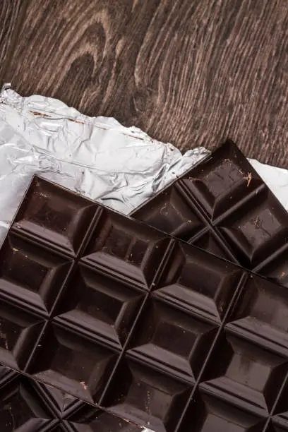 Dark Chocolate bars on foil and brown wooden background