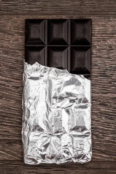 Dark Chocolate bars on foil and brown wooden background