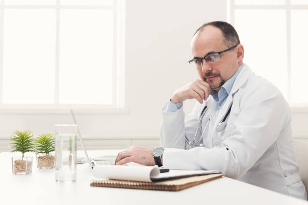 istock Serious doctor in glasses typing on laptop 942191432