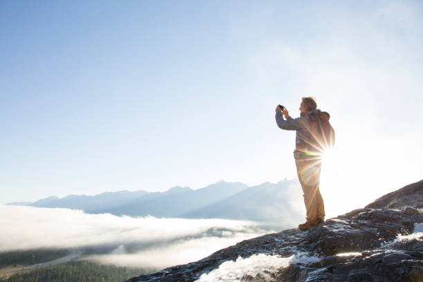 bergsteiger nimmt smartphone-pic über berge, sonnenaufgang - travel destinations mountain hiking profile stock-fotos und bilder