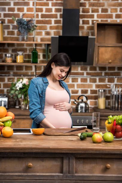 istock happy young pregnant woman touching belly while cooking in kitchen 942209296