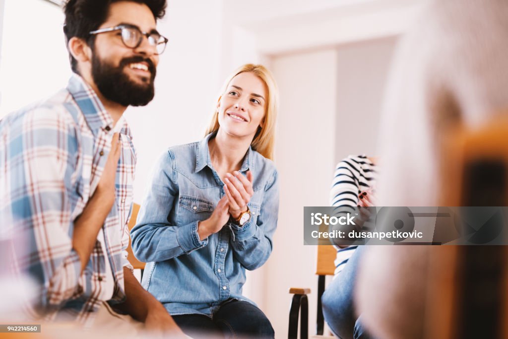 Joven adicto a personas celebrando situación sentado juntos en especial grupo de terapia. Chico guapo hipster sonriente después de su confesión y el progreso. - Foto de stock de Terapia - Tratamiento médico libre de derechos