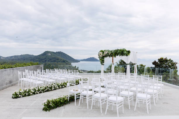 istock Wedding venue setting  on the hill, white chairs with flowers decoration, ocean background 942214588