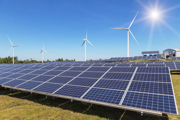 istock Rows array of  polycrystalline silicon solar panels and wind turbines generating electricity in hybrid power plant systems station 942217632