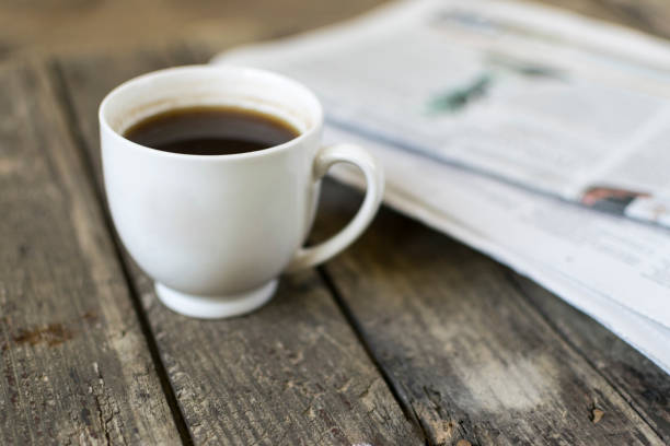 istock White cup of coffee and newspaper on old, wooden table. Selective focus. 942237880