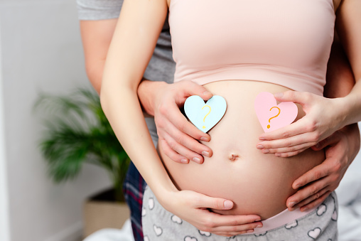 cropped shot of man hugging pregnant woman and holding blue and pink hearts with question marks
