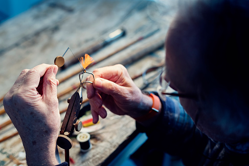 Close up portrait of a fly fisherman working on preparing a fly in a fly tying vice. Experienced fly fisherman can make their own flies with a few simple tools basing their 'look' of the fly on their local knowledge of the waters they fish.