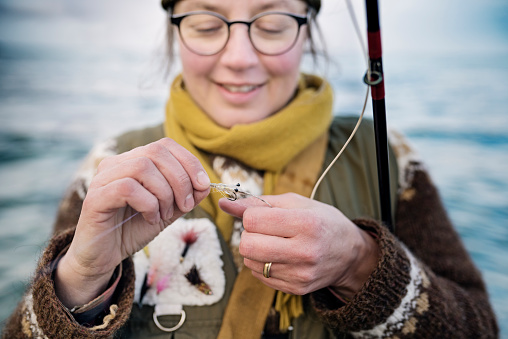 Portrait of a female fisherman  as she carefully ties a fly onto her line. Colour, horizontal format with some copy space. Photographed on location at Nordfeld Strand on the island of Møn in Denmark.