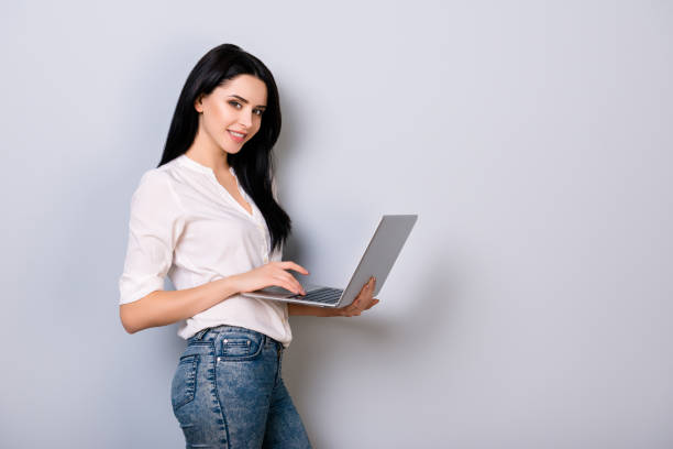 istock Happy young woman in casual clothes using laptop and checkin while standing on gray background 942254952