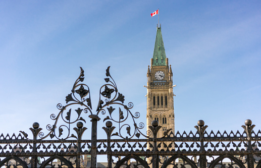 Ornate wrought iron gates in front of Canada's parliament building, with the Canadian flag flying on top of the tower.