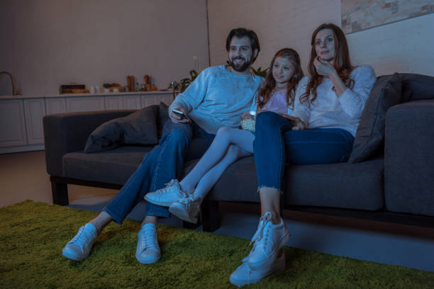 istock smiling parents and daughter watching tv with popcorn 942267208
