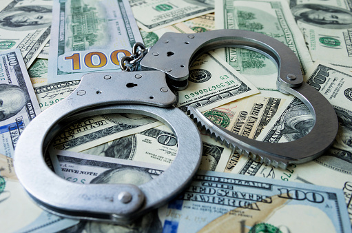 Handcuffs on a pile of US dollar banknotes- symbolic image of a bribe, laundering of money or corruption. Selective focus.