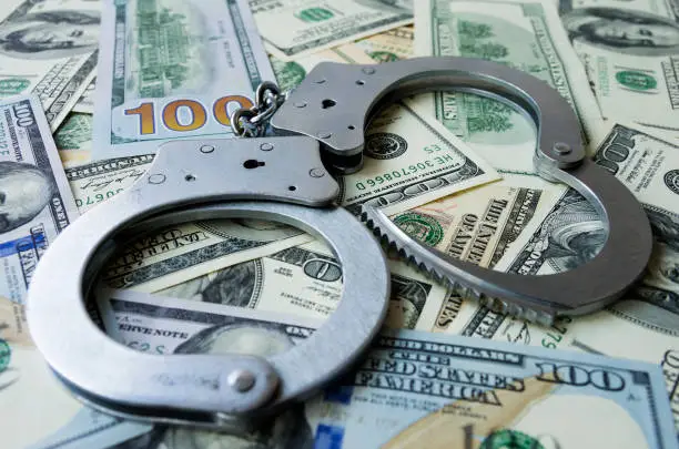 Photo of Handcuffs on a pile of US dollar banknotes- symbolic image of a bribe, laundering of money or corruption. Selective focus.