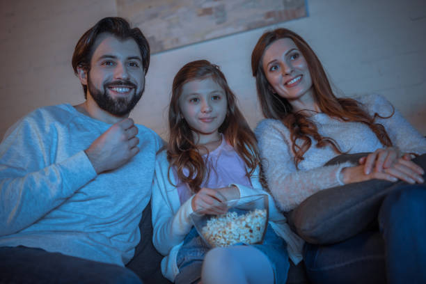 istock happy parents and daughter watching tv with popcorn 942282180