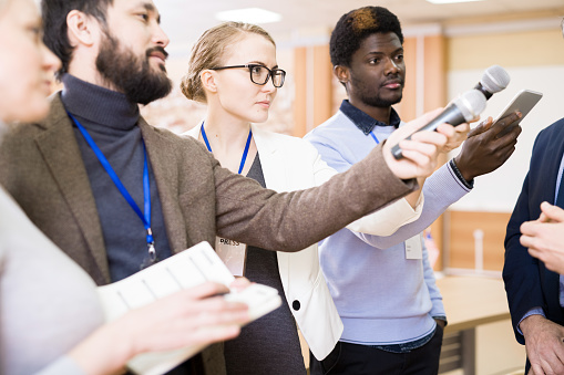 Multi-ethnic group of journalists stretching smartphones and microphones