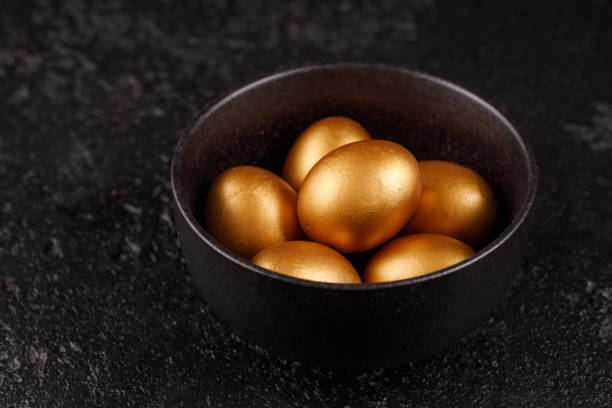 Golden eggs in a black cup on a black textured background. Easter eggs. Eggs, painted in gold for the holiday. stock photo