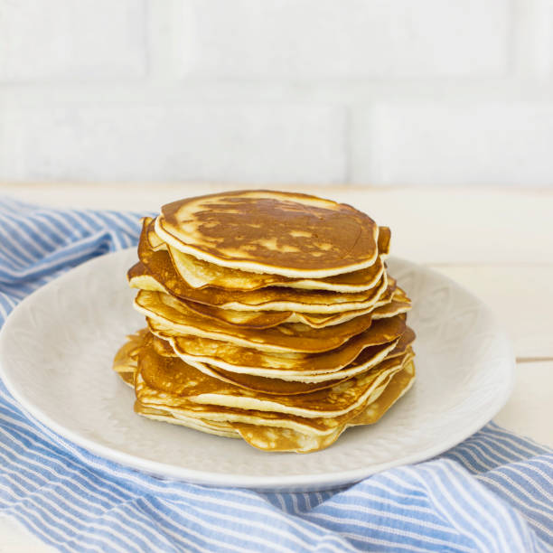 istock Stack of fresh baked pancakes in white plate on blue linen on white background 942283712