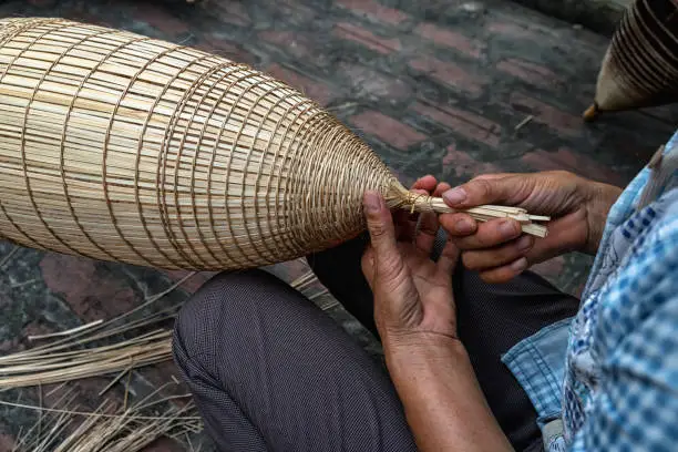 Photo of Closeup Old Vietnamese female craftsman hands making the traditional bamboo fish trap or weave at the old traditional house in Thu sy trade village, Hung Yen, Vietnam, traditional artist concept