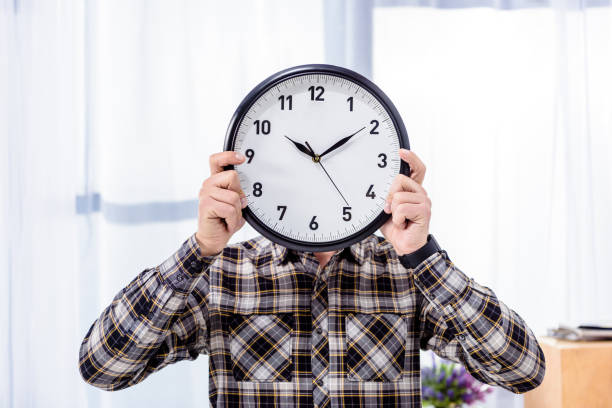 istock Man holding clock over face in front of window 942293308