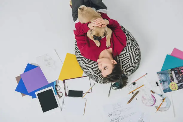 Photo of Young woman lying with pug among sketches