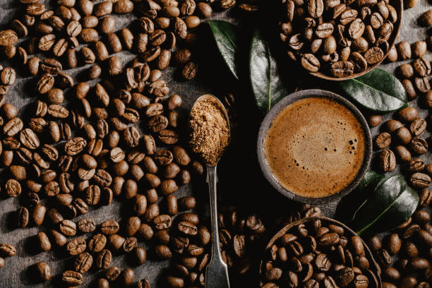 Brewed black coffee and beans in arrangement Top view of cup of brewed black coffee arranged with plenty of brown beans and green coffee leaves. espresso photos stock pictures, royalty-free photos & images