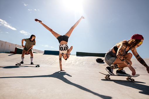 Woman doing flip with female friends skateboarding at skate park. Group of female enjoying at skate park.