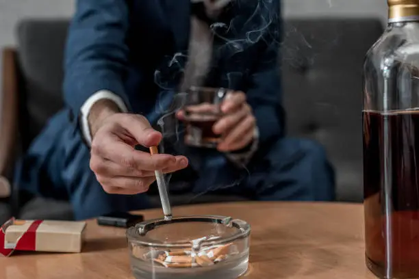 cropped shot of businessman with glass of whiskey and cigarette