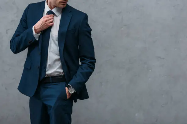 Photo of cropped shot of handsome businessman in stylish suit in front of concrete wall