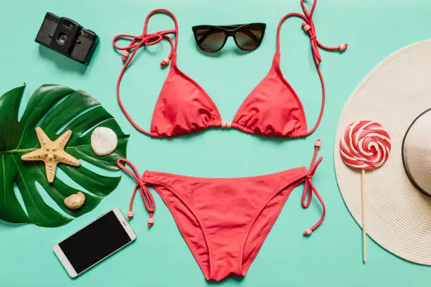 Red, pink bikini suit, lollipop, sunglasses, smartphone, film camera, hat on plain light cyan background. Empty space for copy, text, lettering. Summer vacation concept.